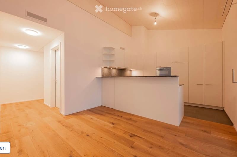 Modern kitchen with white cabinets, a countertop, and an oven. The floor is made of light wooden planks, and the walls are white.