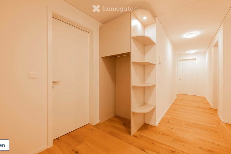 Clean, modern hallway with light wooden flooring, white walls, built-in shelving unit, and recessed lighting.