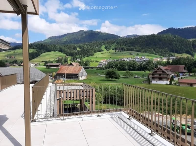 Balcony with a scenic mountain view, surrounded by a rural landscape with houses and green fields.