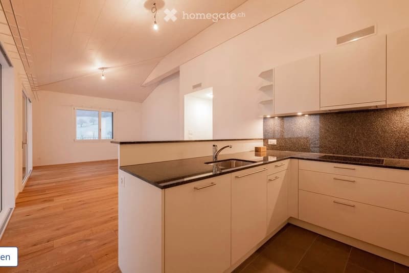 Modern kitchen with white cabinets, black countertops, and a stainless steel sink. The space features wooden flooring and large windows letting in natural light.