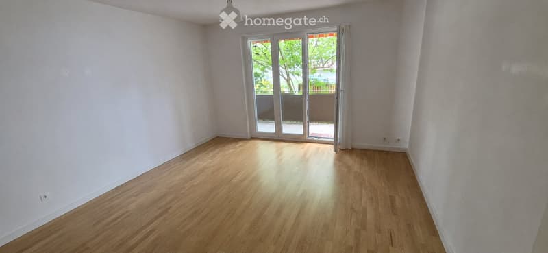 Empty room with wooden flooring, white walls, and large sliding glass doors leading to a balcony.