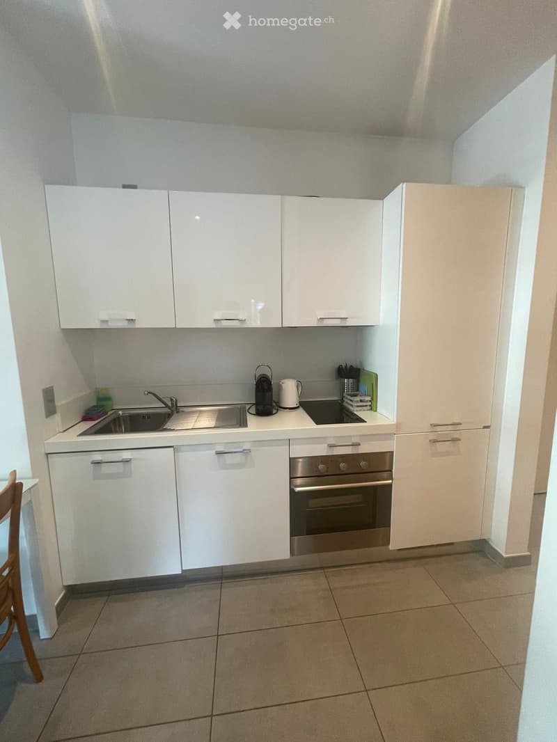 Modern kitchen with white cabinets, stainless steel sink, oven, and countertop appliances including a coffee maker and kettle.