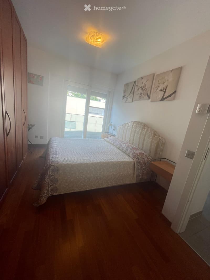 Cozy bedroom with wooden flooring, a neatly made bed, a nightstand, a wardrobe, and artwork on the wall.