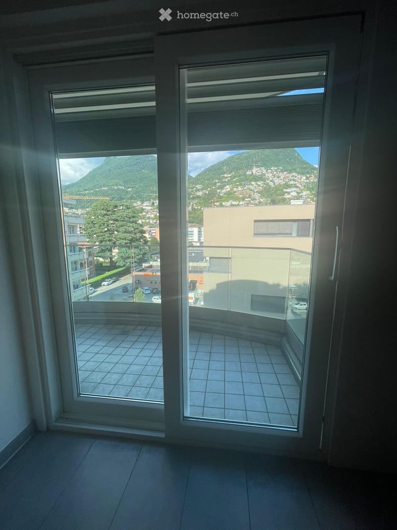 Empty room with large windows offering a scenic mountain and city view, tiled floor, and glass balcony doors.