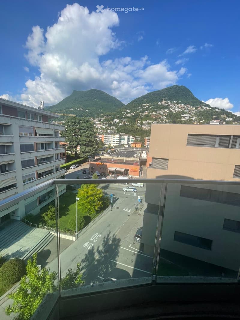 Balcony with a scenic view of a cityscape, mountains, and surrounding buildings under a partly cloudy sky.