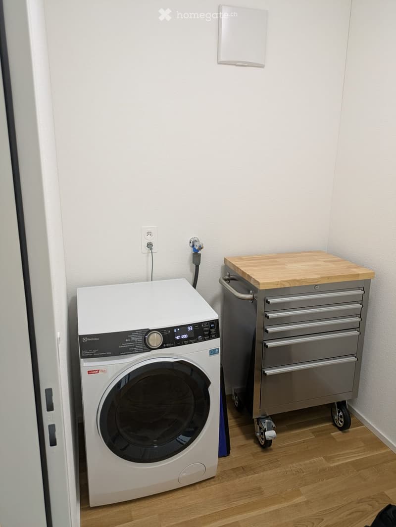 A small bathroom with a white washing machine and a tool cabinet with a wooden top.