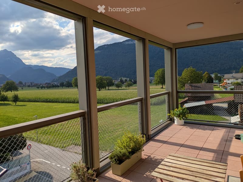 Balcony with wooden bench, potted plants, and scenic mountain and valley view.