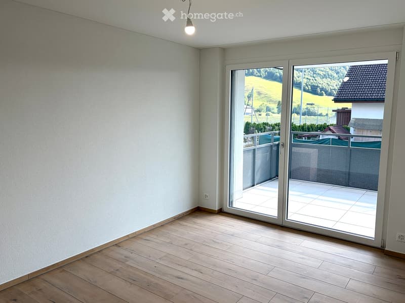 Empty room with wooden flooring, white walls, and large sliding glass doors leading to a balcony with a scenic view.