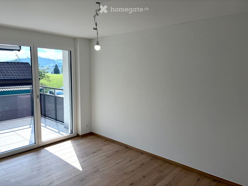 Empty room with wooden flooring, white walls, large sliding glass door leading to a balcony, and a visible outdoor view.