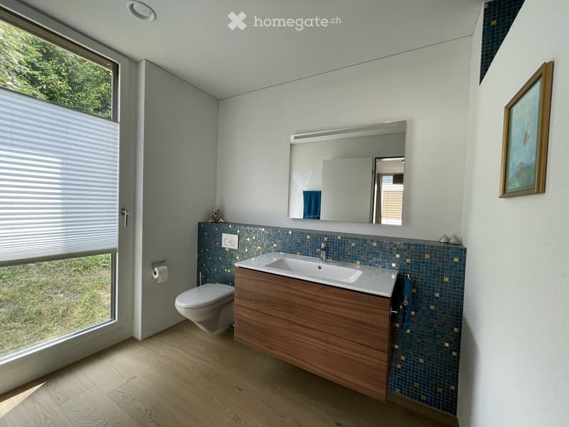 Modern bathroom with a wooden vanity, white sink, large mirror, toilet, and blue mosaic tiles on the backsplash.