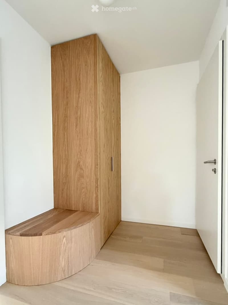 Modern hallway with light wooden flooring, white walls, and a built-in wooden bench and cabinet.