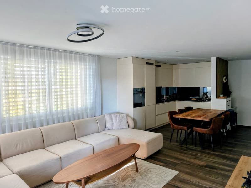 Modern living and dining area with a white sectional sofa, wooden coffee table, dining table with chairs, and a sleek kitchen area with cabinets and appliances.