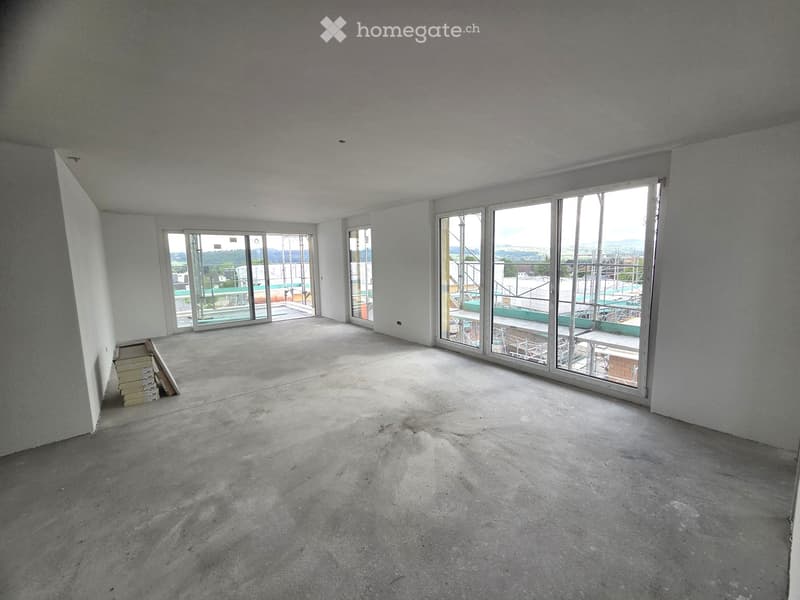 Empty room with concrete floor, white walls, large glass sliding doors leading to a balcony area, and a stack of wooden planks in the corner.