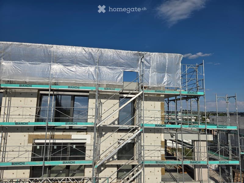 Multi-story building under construction with scaffolding, visible windows, and a covered roof area.