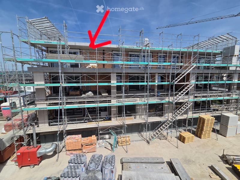 A multi-story building under construction with scaffolding, a red arrow pointing to the top, and various construction materials and equipment on the ground.
