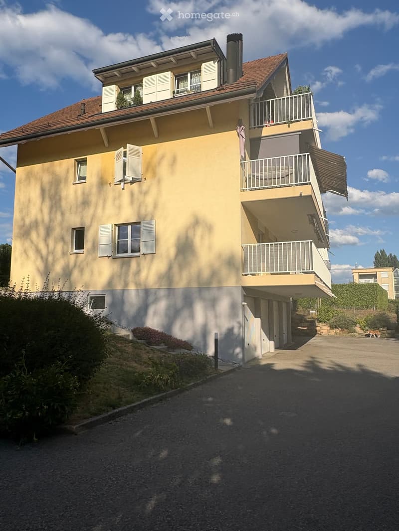 Two-story house with beige walls, red-tiled roof, multiple windows with shutters, balconies, and a driveway.