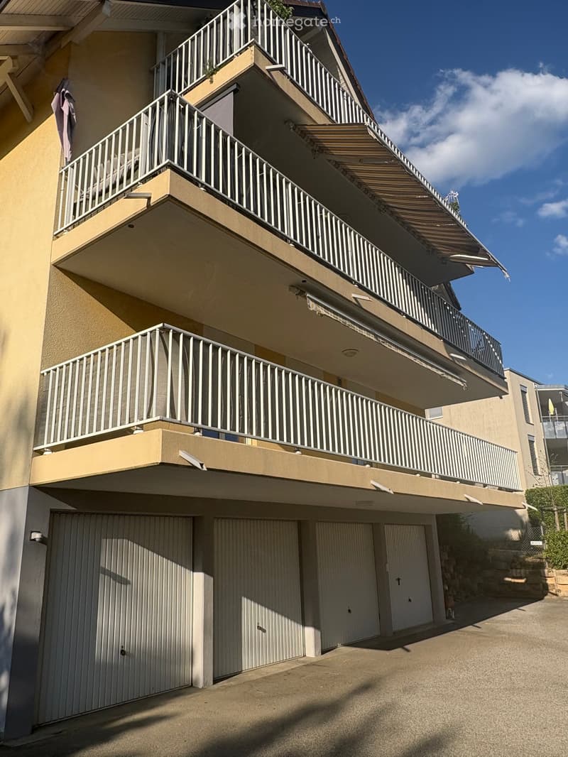 Multi-story residential building with multiple balconies, beige exterior, and garage area.