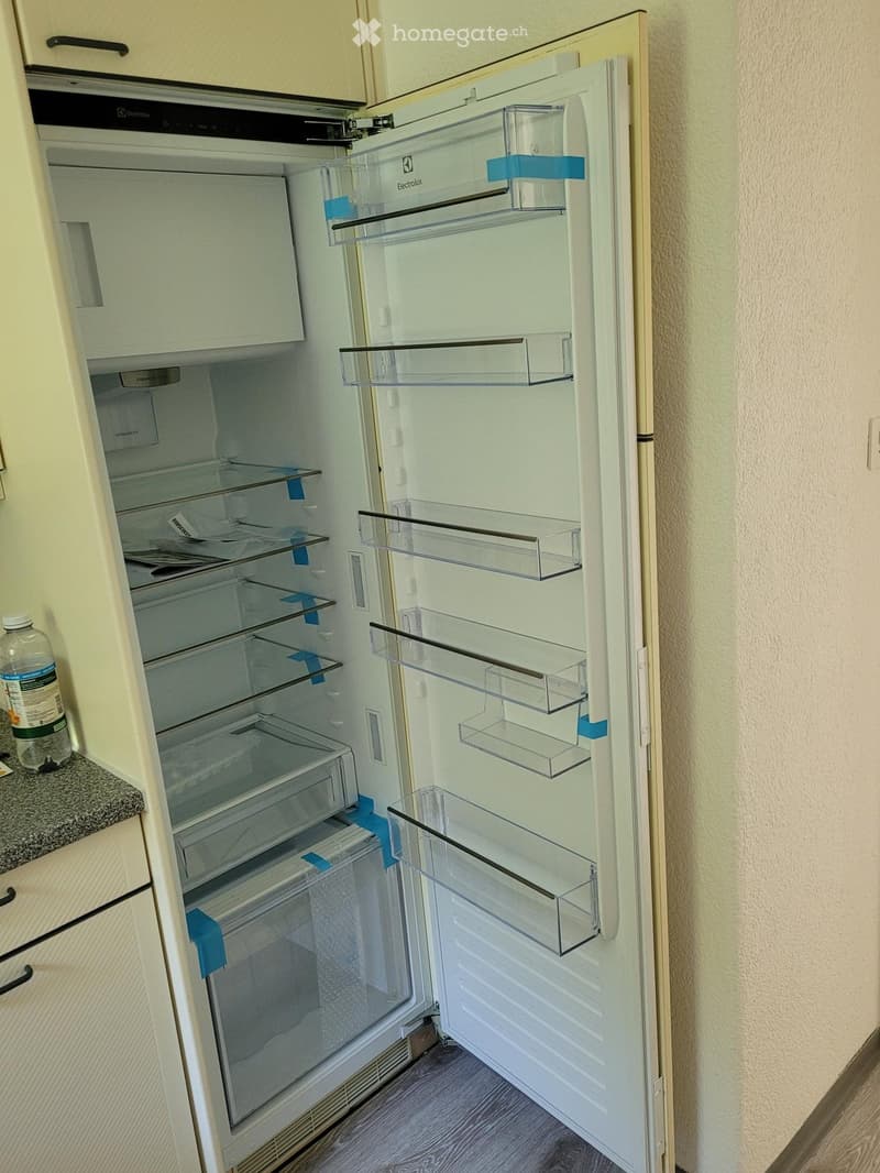 Open refrigerator with multiple glass shelves and drawers, placed in a kitchen with light-colored cabinets and a granite countertop.