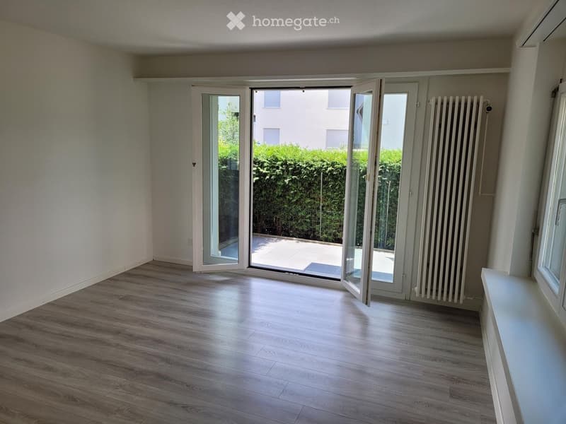 Empty room with wooden flooring, white walls, large sliding glass doors leading to a balcony, and a radiator on one wall.