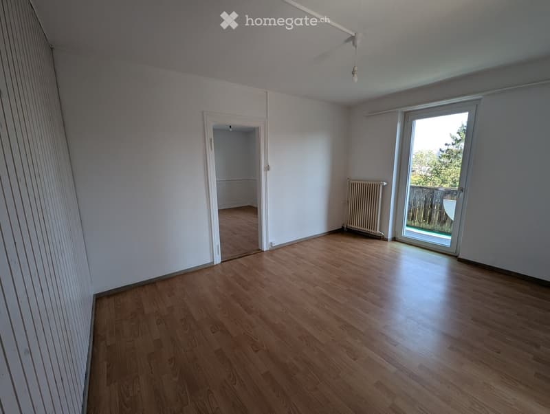 Empty room with wooden flooring, white walls, a radiator, and a sliding glass door leading to a balcony.