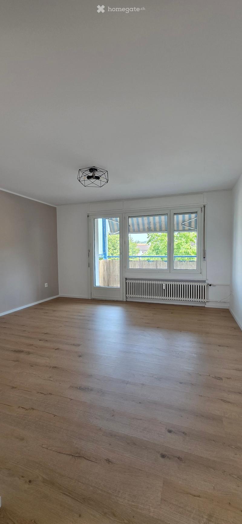 Empty room with wooden flooring, white walls, large windows, and a radiator. No furniture or equipment present.