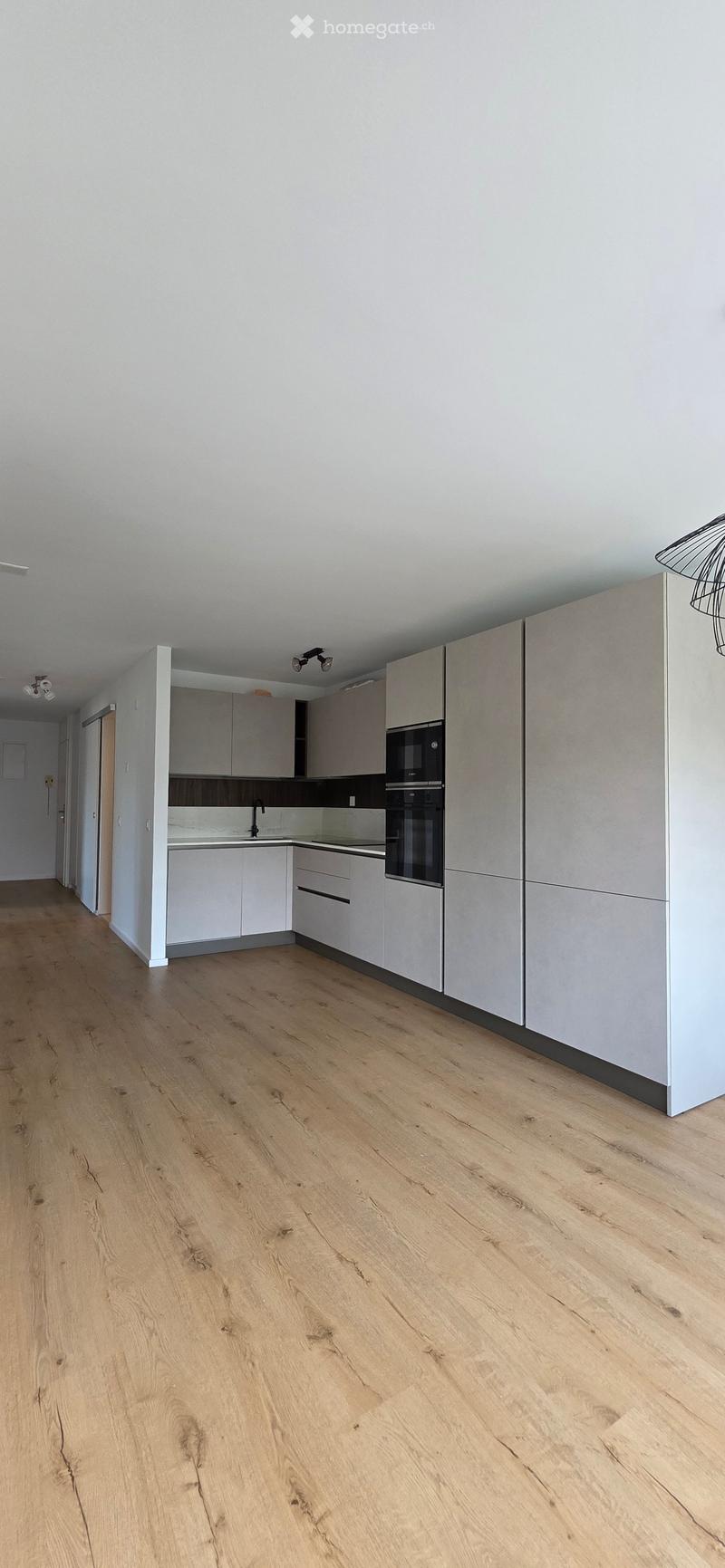 Modern kitchen with light grey cabinets, a sink, a microwave, and an oven. The floor is made of light wooden planks.