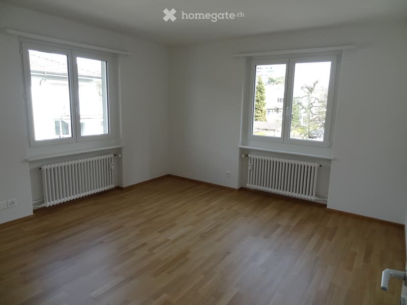 Empty room with wooden flooring, white walls, and two windows with radiators beneath them.