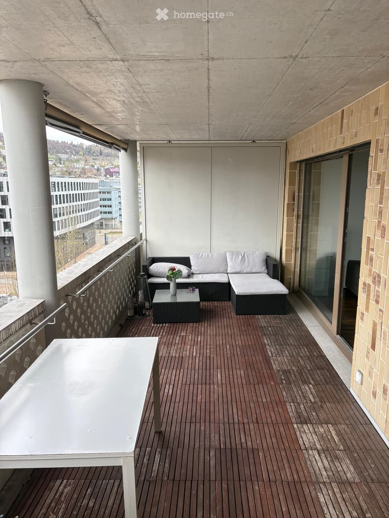 Balcony with wooden decking, white sofa, coffee table, and a white table near the railing.