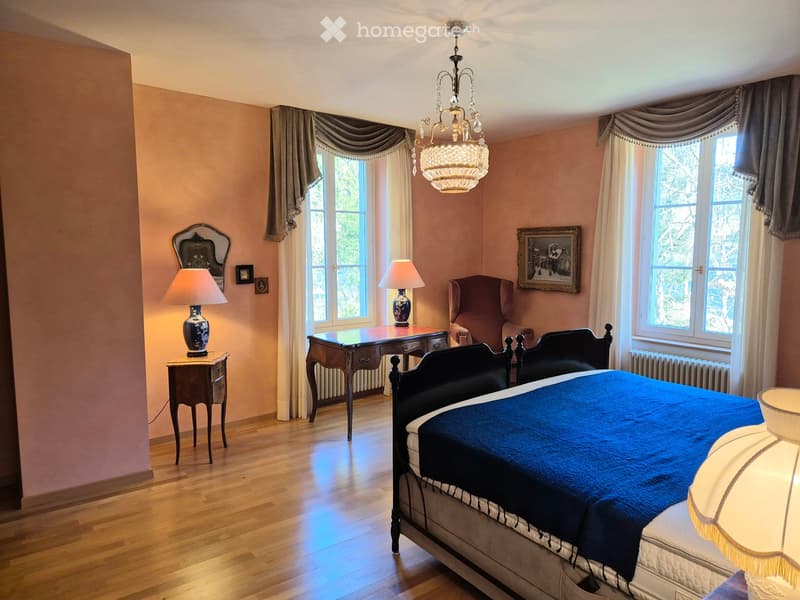 spacious bedroom with two beds, pink walls, wooden floor, chandelier, lamps, desk, armchair, windows, radiator, pictures