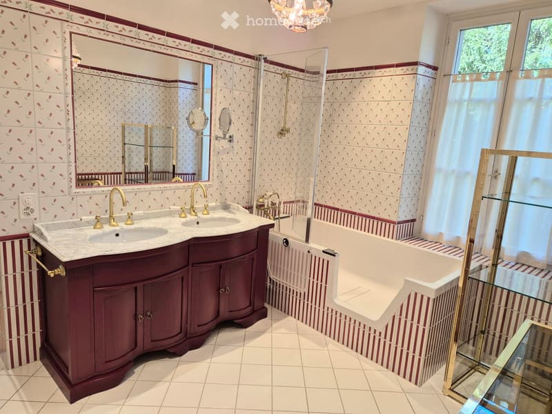 Elegant bathroom with a double sink vanity, marble countertop, brass fixtures, a large bathtub with a glass enclosure, and decorative tiles.