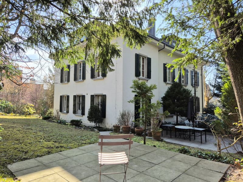 Three story white house, multiple windows, garden, pathway, potted plants, outdoor table and chairs