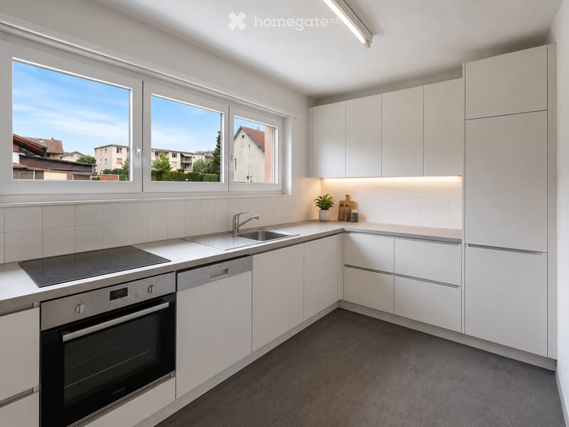 Modern kitchen with white cabinets, stainless steel appliances, and a large window overlooking a residential area.