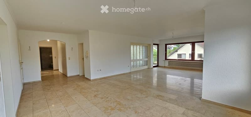 Empty room with tiled floor, white walls, large windows, and a doorway leading to another room.