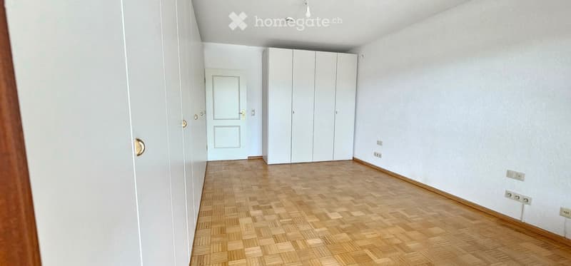 Empty room with light-colored walls, wooden herringbone flooring, and built-in white closet units. No furniture or personal items are present.