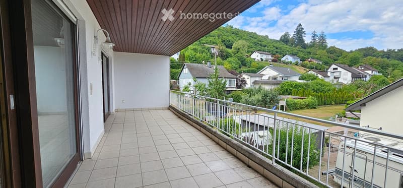 Balcony with tiled floor, wooden ceiling, metal railing, overlooking a residential area with houses and greenery.