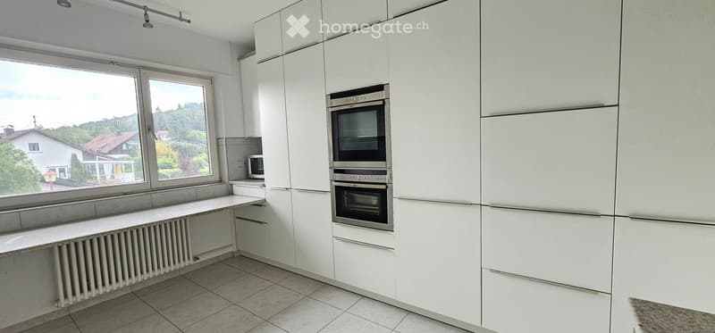 Modern kitchen with white cabinets, built-in oven, microwave, and large windows overlooking a scenic view.