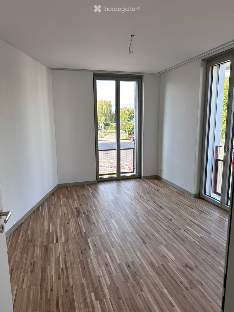 Empty room with wooden flooring, white walls, and large glass sliding doors leading to an outdoor area.