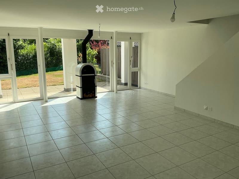 Empty room with tiled floor, white walls, large glass doors leading to outdoor area, and a wood-burning stove in the center.