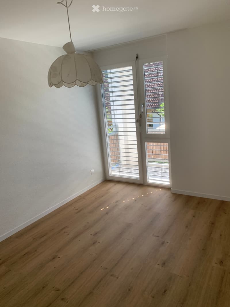 Empty room with white walls, wooden floor, and a glass door leading to a balcony.