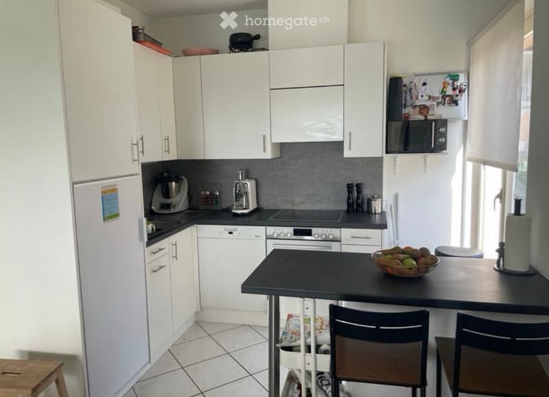 Modern kitchen with white cabinets, stainless steel appliances, and a black island with a fruit bowl and chairs.