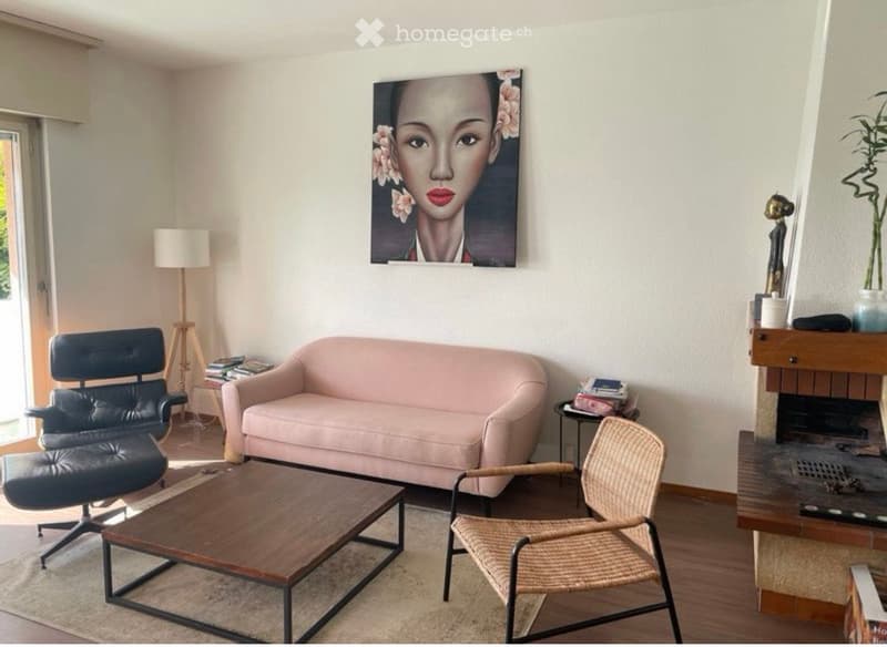 Modern living room with a pink sofa, wooden coffee table, black leather chair, wicker chair, floor lamp, fireplace, and artwork on the wall.