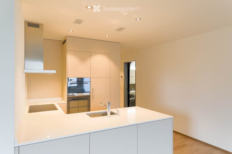 Modern kitchen with light-colored cabinets, a white countertop, a stainless steel sink, and an oven. The space features recessed lighting and a sleek design.