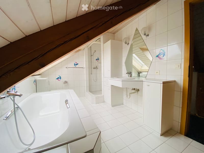 Modern bathroom with a bathtub, sink, mirror, and shower area. The room features white tiles and wooden beams on the ceiling.