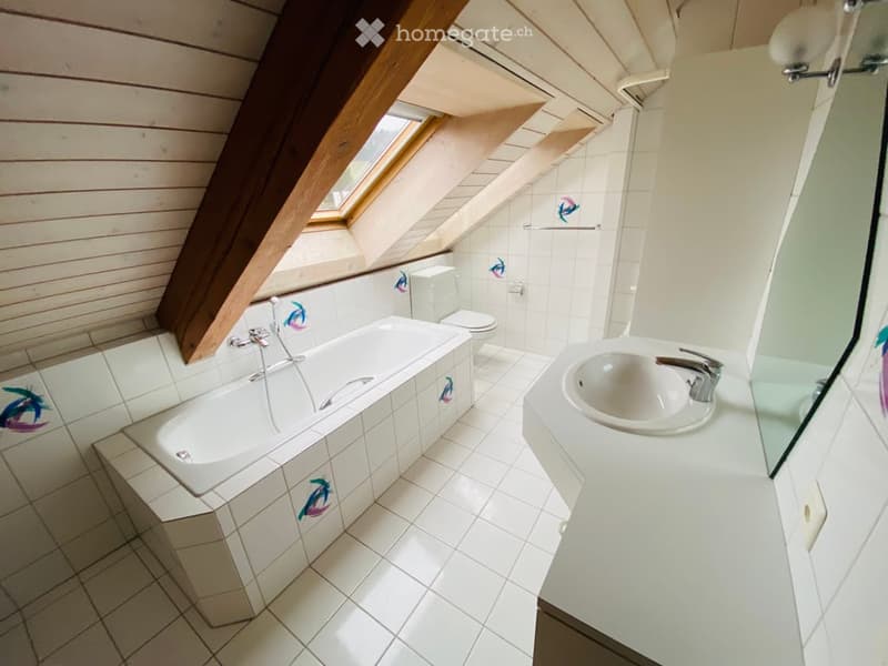 Bright bathroom with white tiled walls and floor, featuring a bathtub, toilet, sink, and a large window letting in natural light.