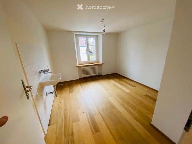 Empty bathroom with wooden flooring, white walls, a window, a radiator, and a sink.