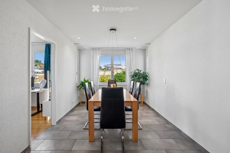 Modern dining room with a wooden dining table, black chairs, pendant light, and plants near the windows.