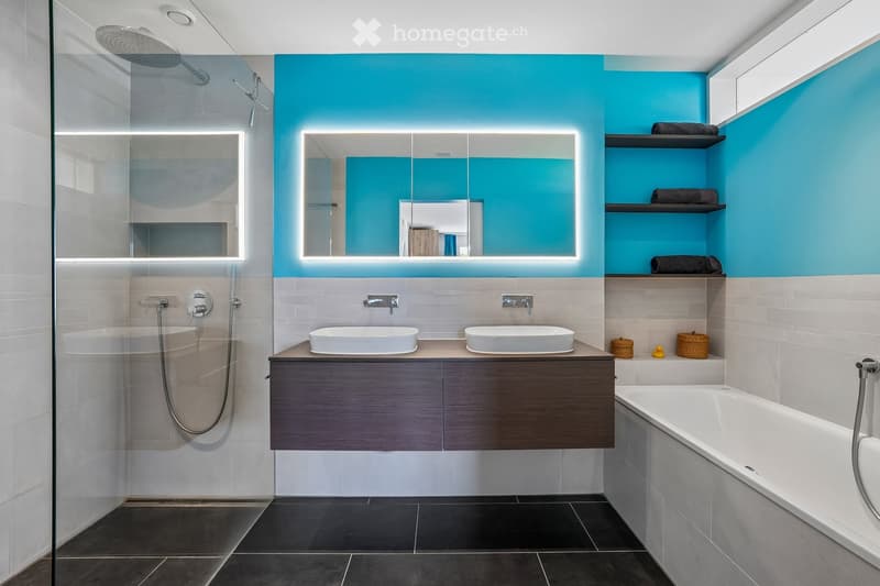 Modern bathroom with a bathtub, double sink, illuminated mirrors, and a glass-enclosed shower area.