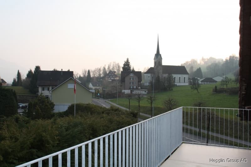 Balcony overlooking a rural village with houses, a church, and green fields.
