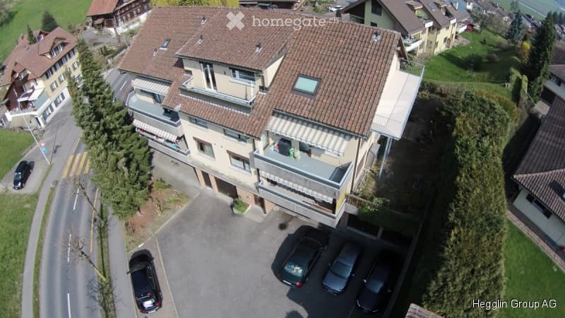 Aerial view of a multi-story residential building with a tiled roof, balconies, and a parking area with several cars.