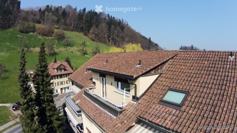 View of a multi-story residential building with a red-tiled roof and a scenic hillside background.